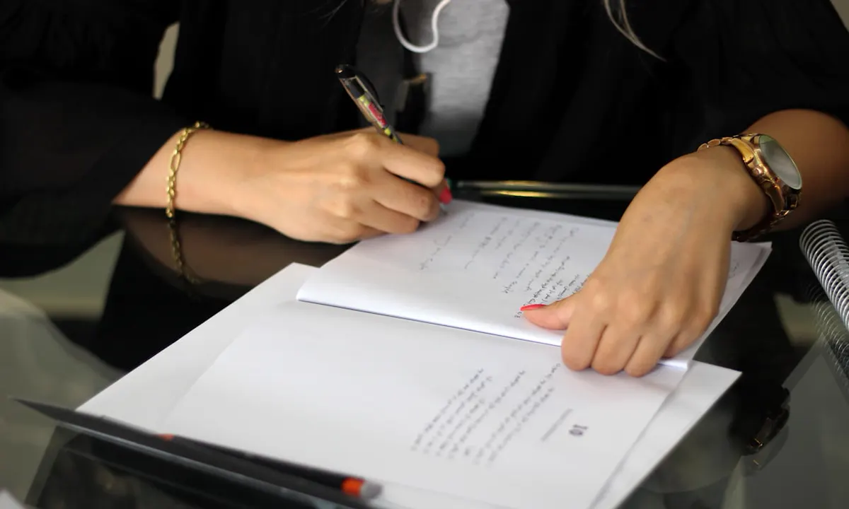 Une main remplit à la plume des formulaires fiscaux posés sur un bureau en verre